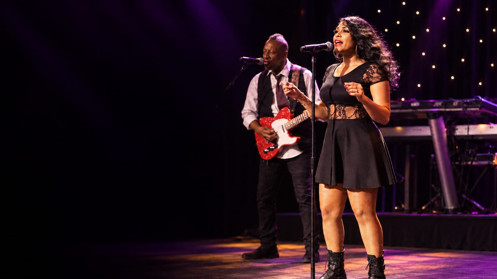 Seven singing on stage with her band behind her.