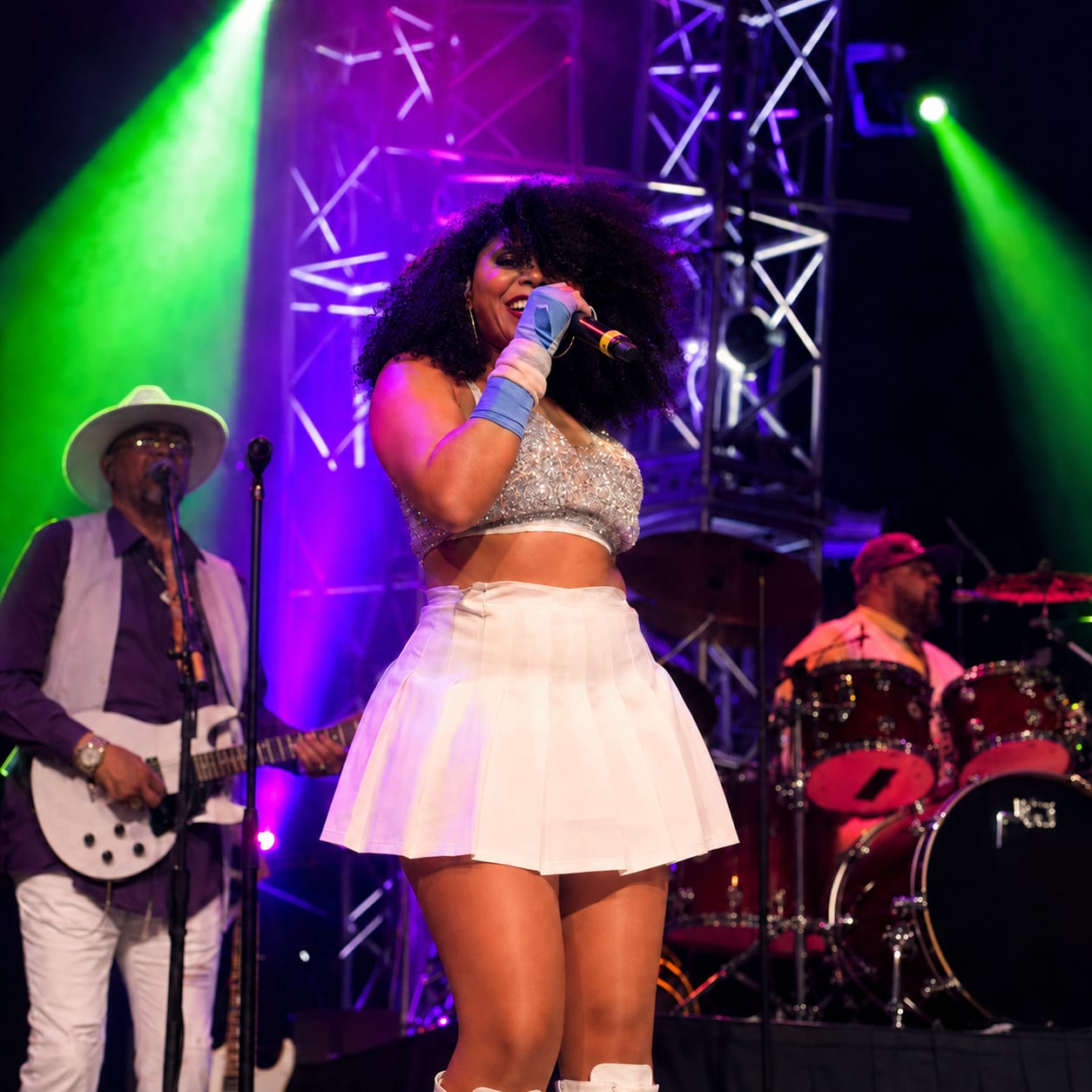 Seven mid-song on stage under green and purple light, her band playing behind.