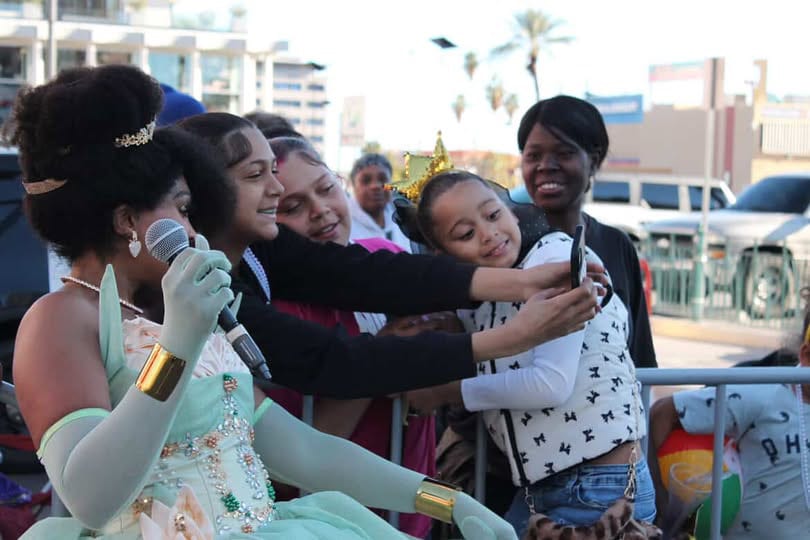 Singing to a group of children outdoors, several of them leaning in for a hug.