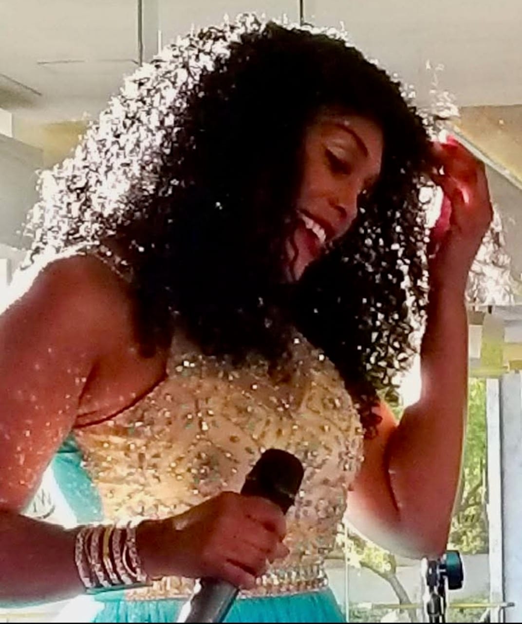 Singing into a handheld microphone in a gold beaded gown.