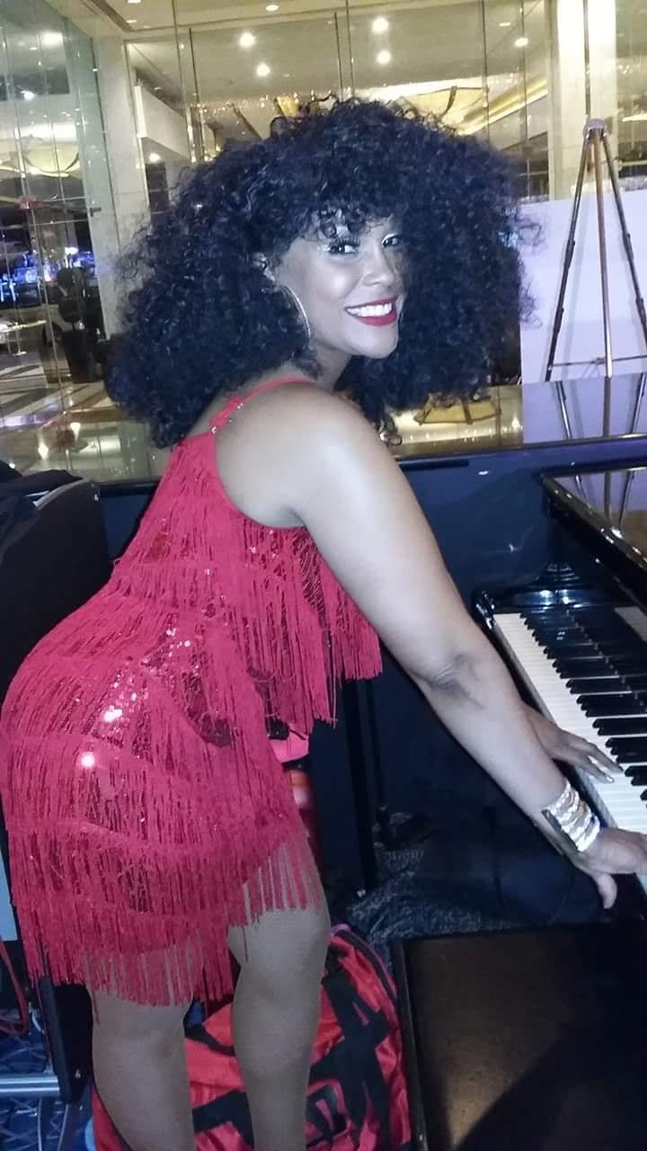 Standing at a piano in a pink fringed dress.