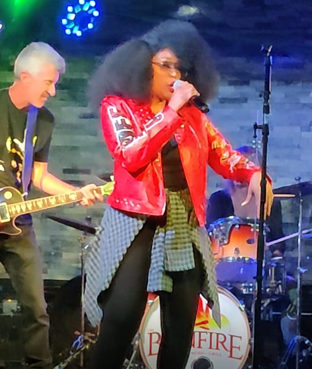Mid-song in a red leather jacket while a guitarist leans in beside her.