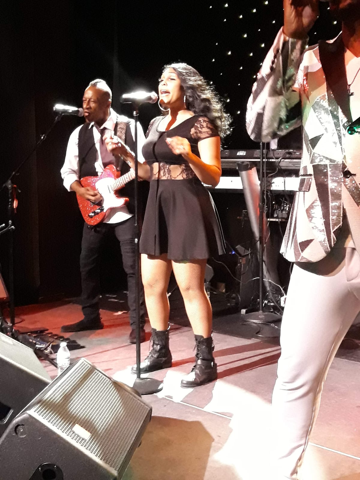 Singing into a microphone on stage, a band playing behind.