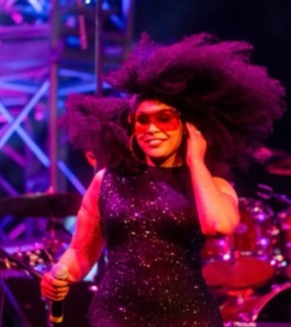 A vocalist mid-song under magenta stage light, hair thrown back, microphone in hand.